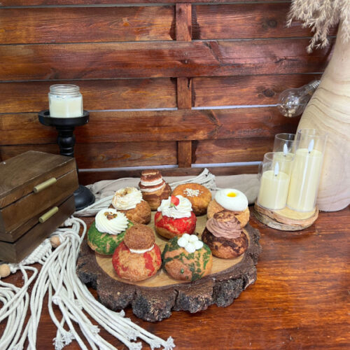 Nouă sortimente de choux prezentate pe un blat de lemn, decor marca Something Sweet
